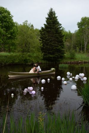 A romantic canoe ride on a pond with floating balloons and evergreen trees in background.