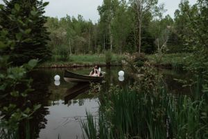 Couple in a wooden canoe on a peaceful pond with white balloons floating on the water.