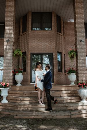 Stylish couple on brick mansion steps with decorative urns and flowers.