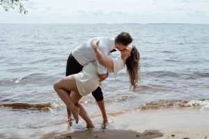 A romantic dance dip pose on the beach with ocean waves in the background.