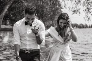 A black and white photo of two people laughing together by the water.