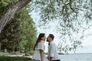 Romantic couple sharing an intimate moment by the lake under overhanging tree branches.