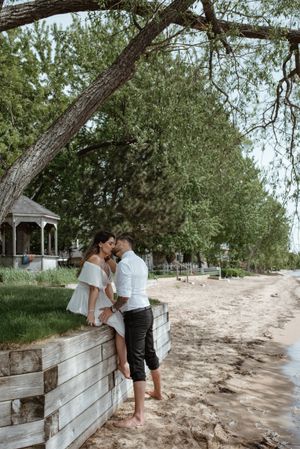 Couple embracing on wooden boardwalk near beach with gazebo in background.