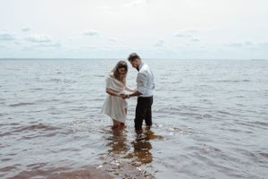 Couple standing together in shallow water at ocean shore during cloudy day.