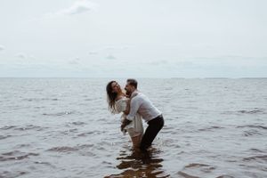 A romantic couple playing and embracing in the ocean water at dusk.