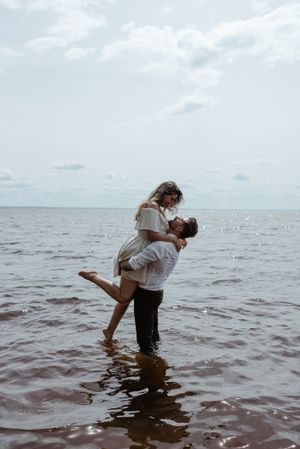 A romantic moment captured of a couple dancing in knee-deep water against an ocean backdrop.