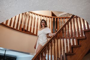 Woman in white dress poses on wooden staircase with natural lighting.