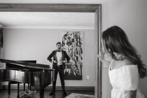 Black and white photo of couple separated by doorway with piano.