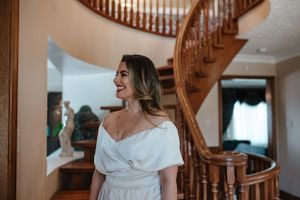 Woman in white dress smiles near curved wooden staircase.