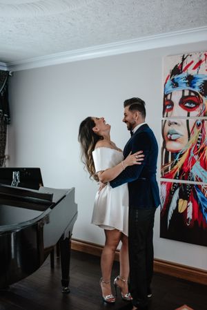 Couple embraces near piano with colorful pop art portrait on wall.
