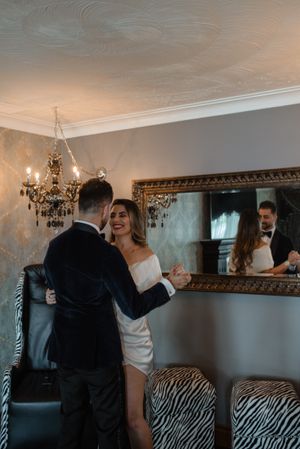Couple dancing together in elegant room with chandelier and ornate mirror.