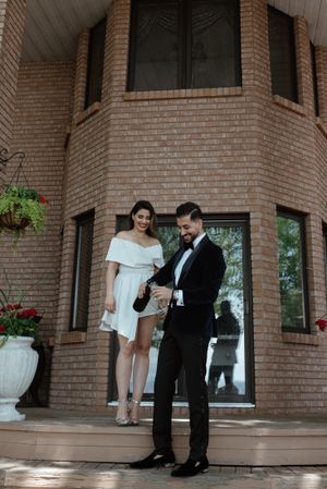 A couple in wedding attire poses on the steps of a brick building with elegant architecture.