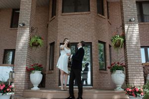 Elegant couple poses in formal attire at brick entrance with decorative urns and hanging plants.