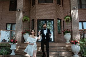 Stylish couple poses on brick steps decorated with floral arrangements and white urns.