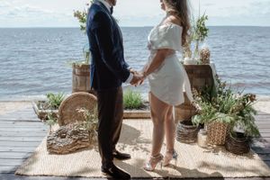 Seaside ceremony setup with couple standing on rug among potted plants.