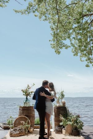A romantic waterfront ceremony setup with wine barrels and floral decorations along a dock overlooking the ocean.