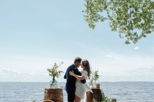 A romantic oceanside moment with rustic barrels and greenery decorations under a bright blue sky.