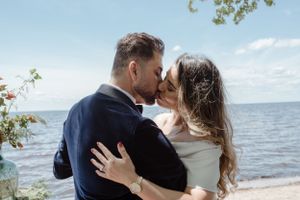 A romantic embrace by the waterfront with trees and blue sky in the background.