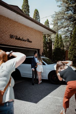 Photographers capturing a moment between two people by a brick building with parked cars.