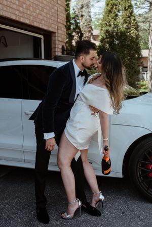 Romantic moment shared between a couple in formal attire next to a white car in a driveway.