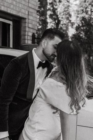 A black and white romantic moment captured between newlyweds next to a car.