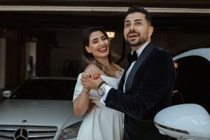 Newlyweds share a joyful moment together by their car after their wedding ceremony.