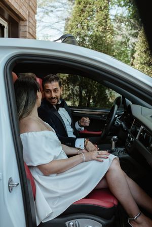 Couple sitting in luxury car interior with white dress and formal attire.