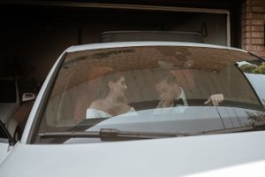 A tender moment shared inside a white car with sunlight streaming through the windshield.