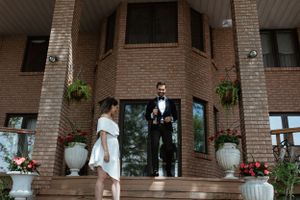 Couple in formal attire standing at entrance of brick building with decorative planters.
