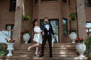 Elegant couple posing on steps of brick building with white floral arrangements.