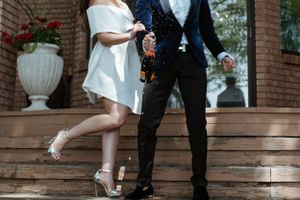 Couple in formal wear striking playful pose on brick steps with decorative urns.