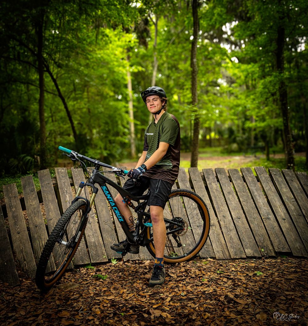Mountain biker with helmet poses with bike on wooden platform in forest.