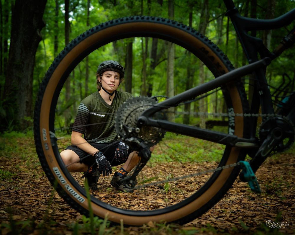 Mountain biker poses with bike wheel in creative forest portrait.