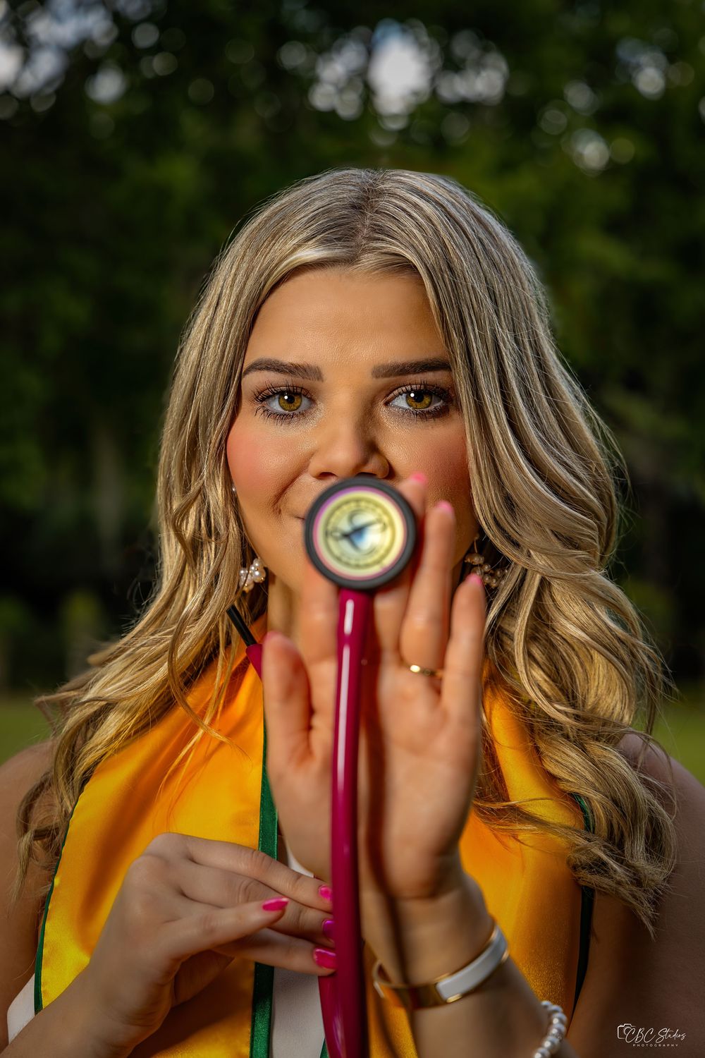 Graduate in yellow stole holds up tassel against face during graduation photo shoot.