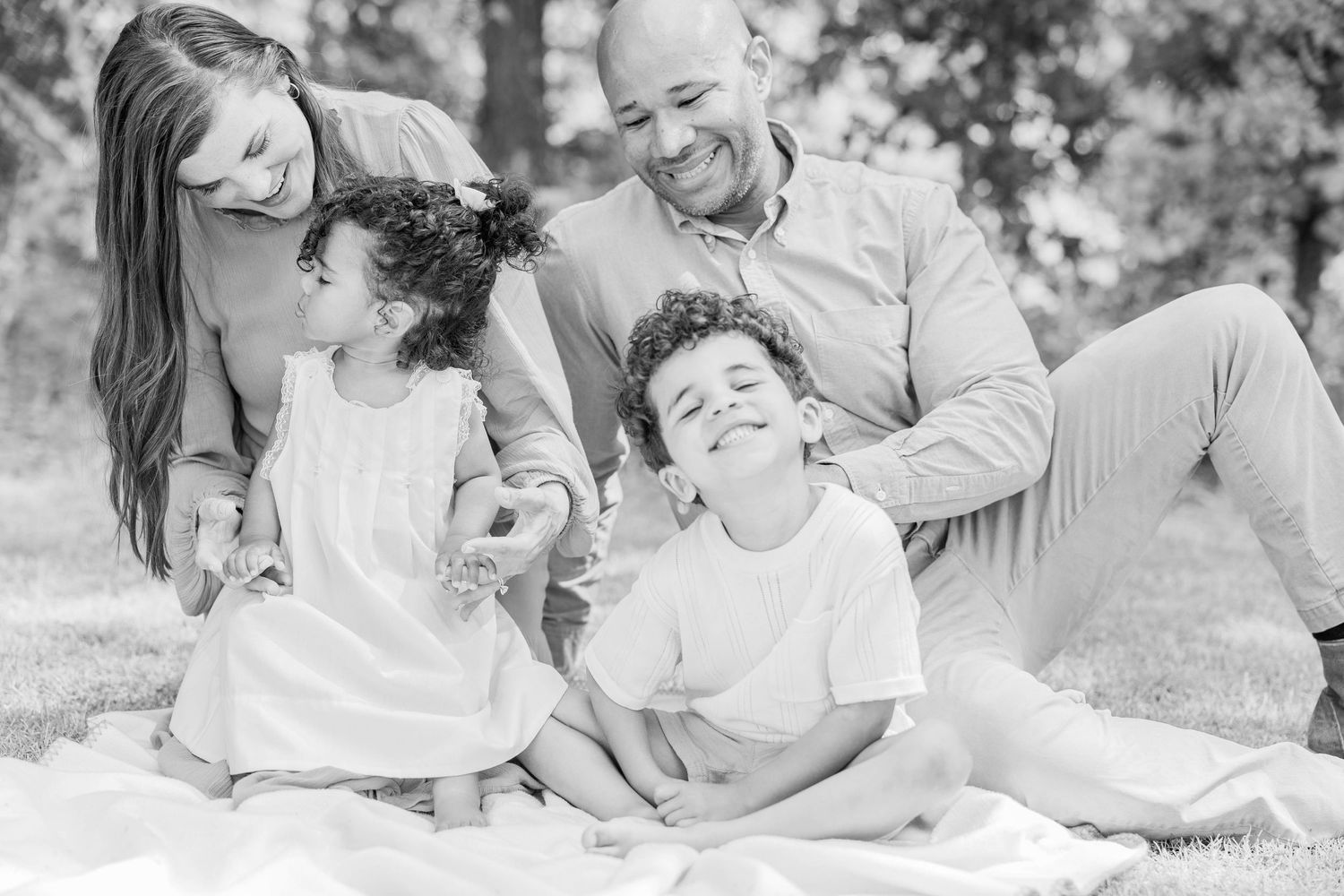 Black and white candid photo of family laughing together during outdoor picnic.