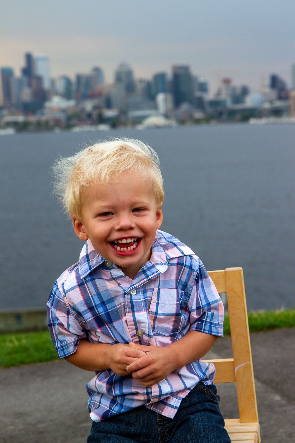 A young child in a plaid shirt laughs joyfully with the Seattle skyline visible across the water in the background.