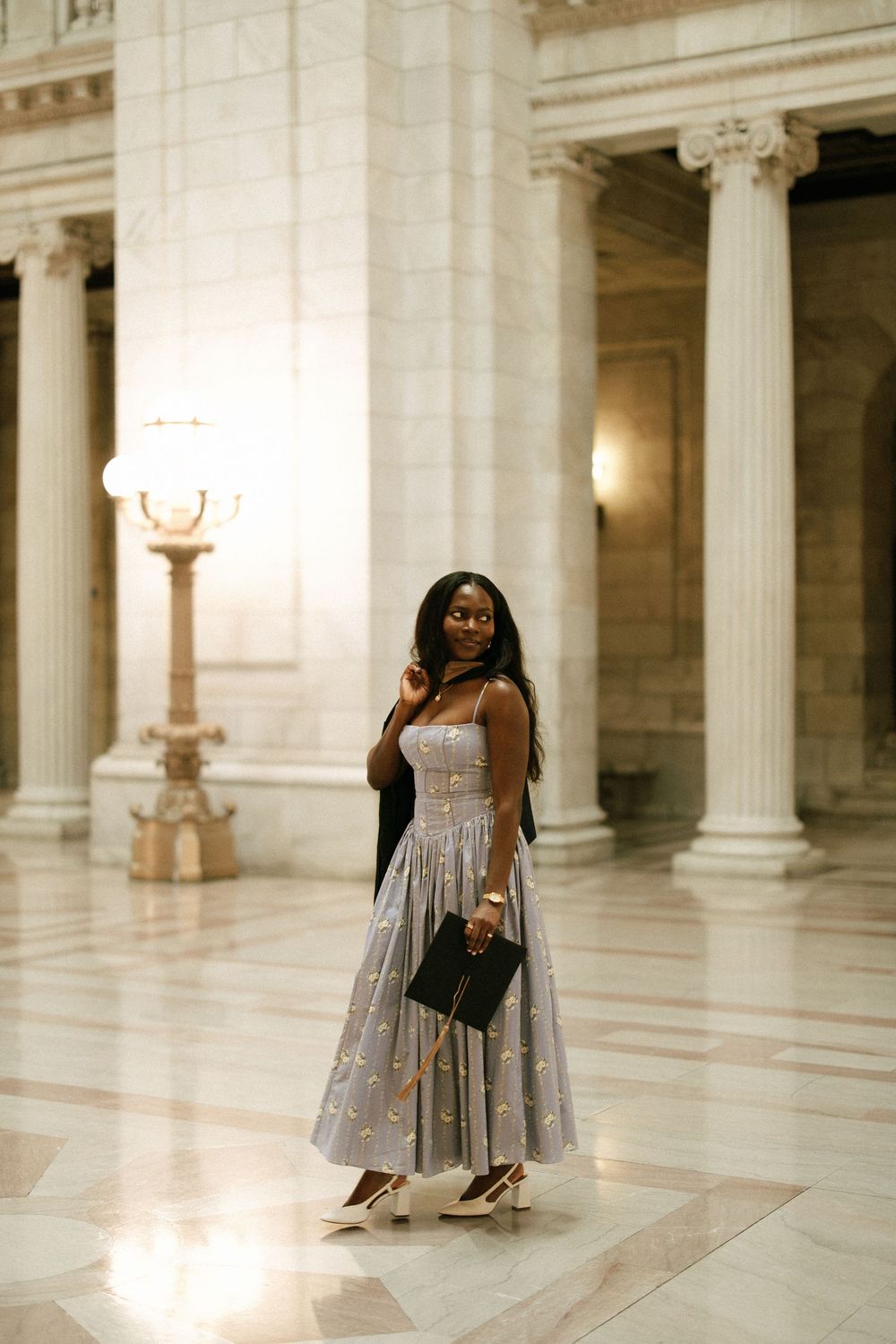 Elegant Black woman in silver floral midi dress poses in grand marble hall with tall columns.