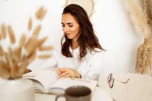 Someone reads a book at a peaceful desk setting with pampas grass decor and a white aesthetic interior.