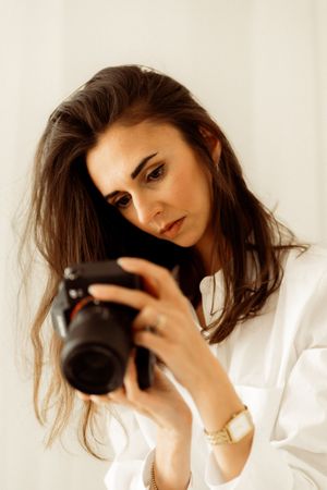 Professional photographer holding a DSLR camera while wearing a white shirt in a light-filled room.