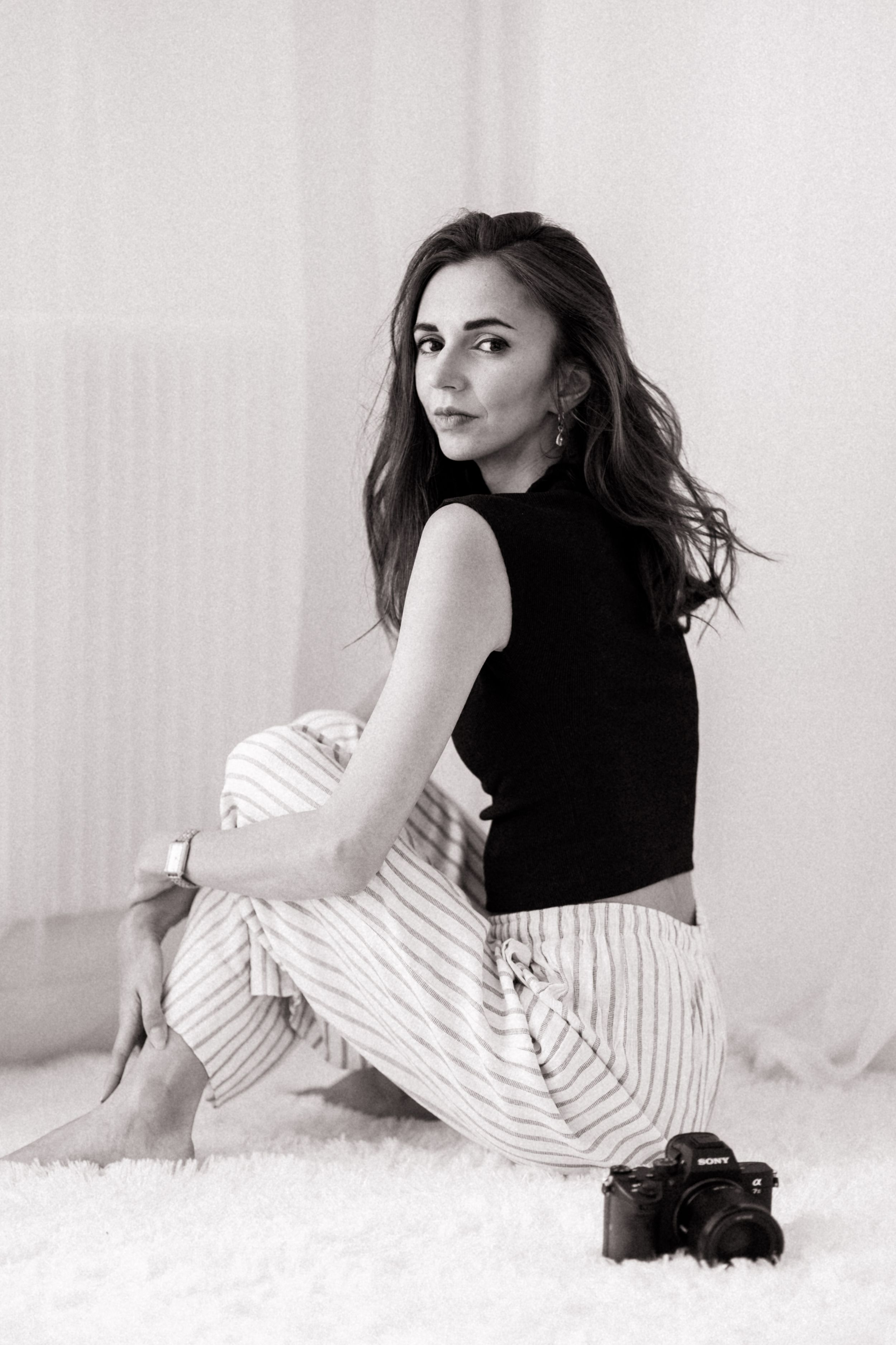 Black and white photo of someone sitting on floor wearing striped skirt and camera nearby.