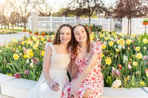 Two people in dresses sitting among yellow and pink tulips in a garden setting at mount timpanogos temple in American Fork, Utah.