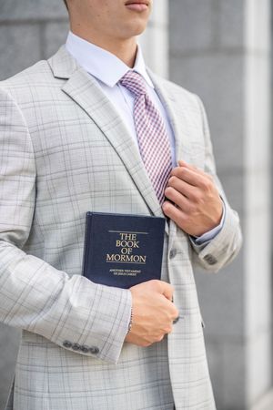 Close-up of a missionary wearing a gray suit and pink tie holding The Book of Mormon.