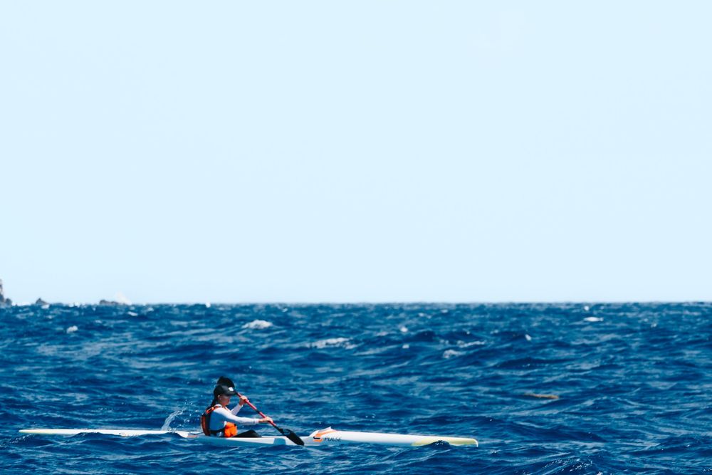 A lone kayaker paddling across deep blue choppy ocean waters on a bright sunny day.