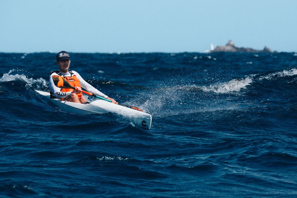 A kayaker in a white kayak navigates through choppy blue ocean waters on a sunny day.