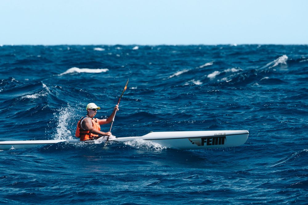A kayaker navigates through choppy blue ocean waters with breaking waves on a sunny day.