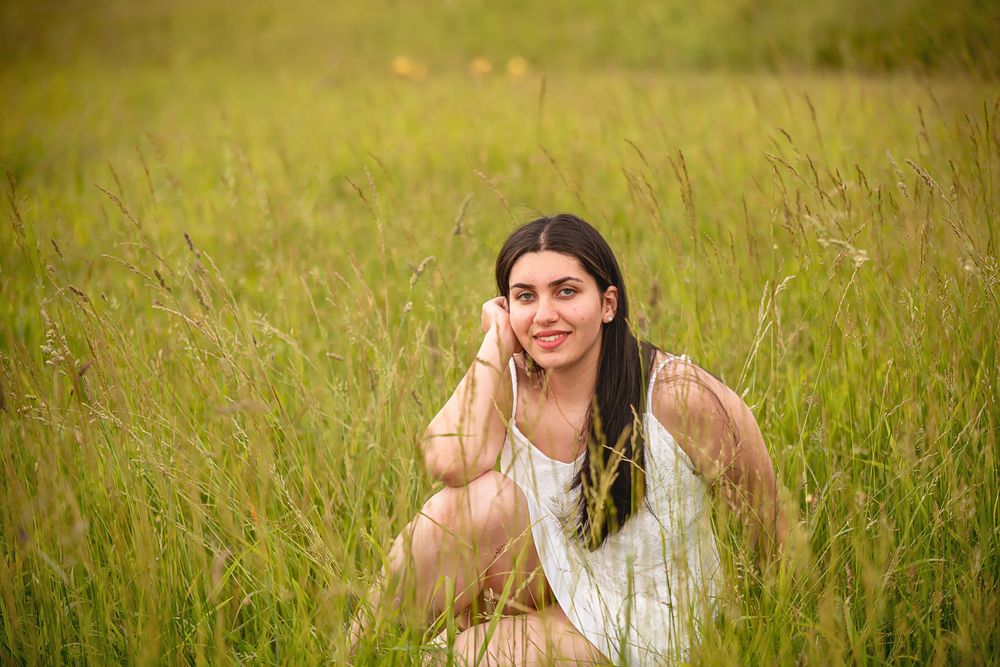 A dreamy portrait of a person in white dress sitting among tall grass in a field.