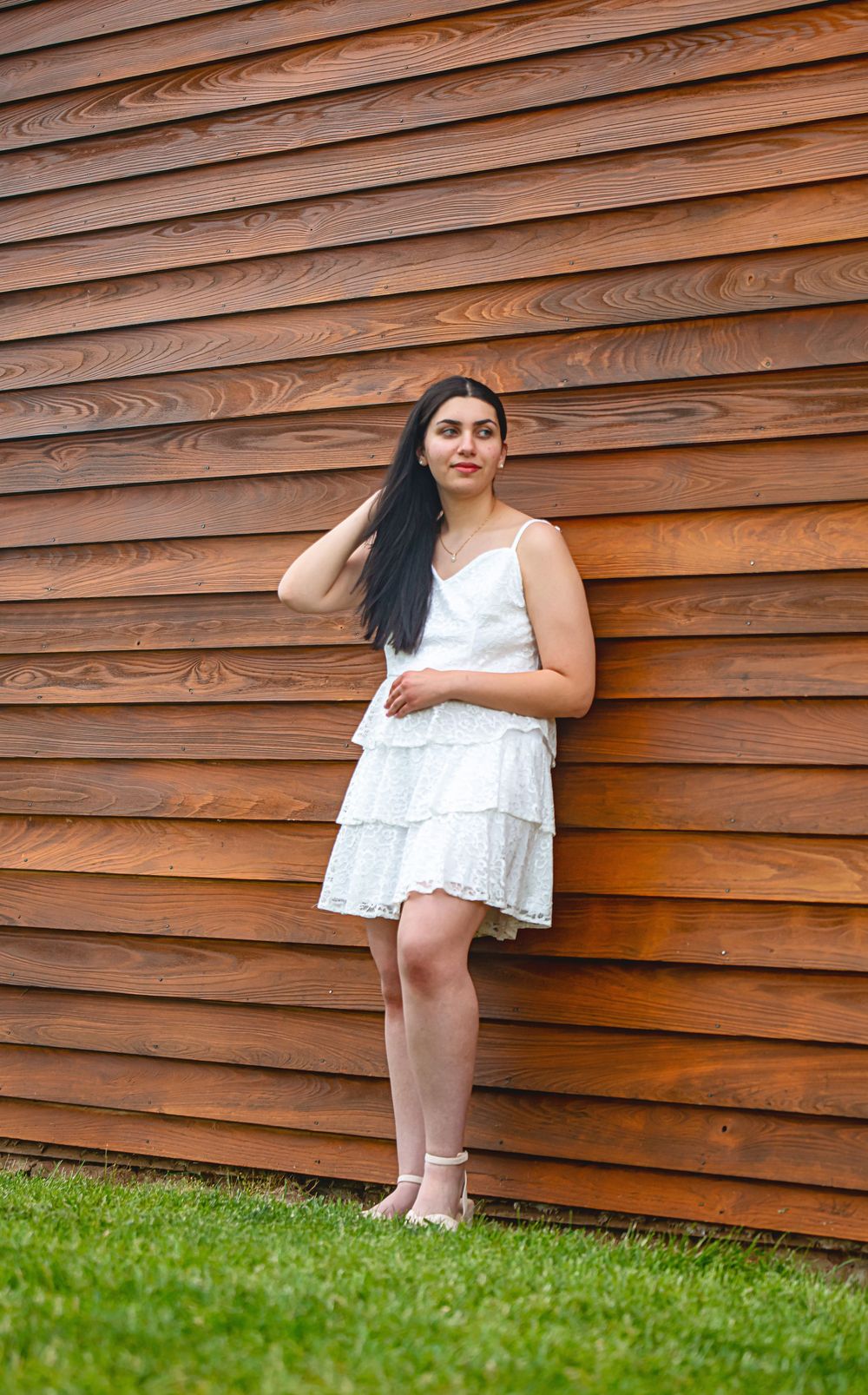 A woman in a white tiered dress poses against a rustic wooden wall.