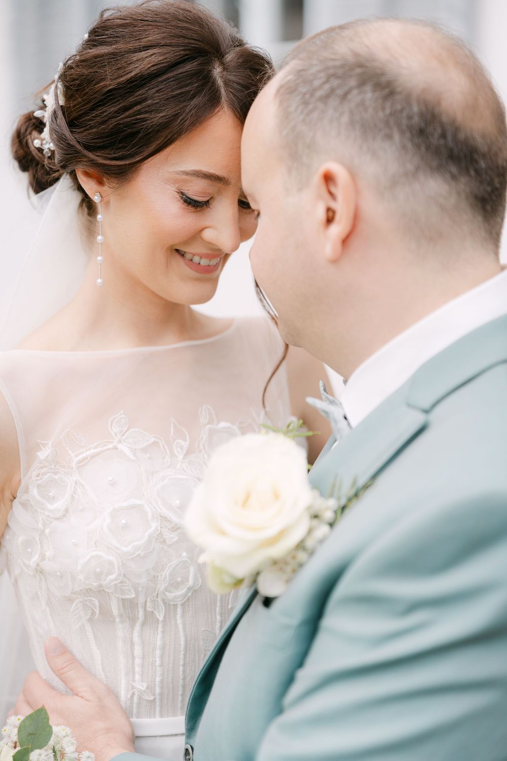A romantic wedding moment captured in soft light as bride and groom share an intimate moment in mint and white attire.