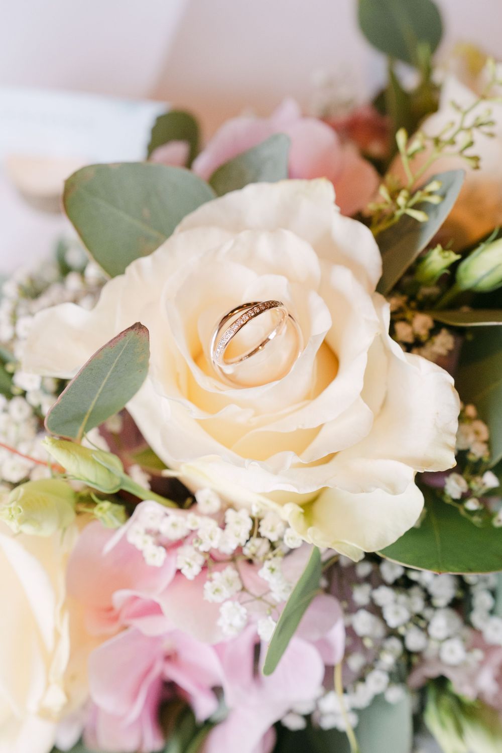 Close-up view of soft cream-colored roses and delicate baby's breath flowers arranged with green eucalyptus leaves.