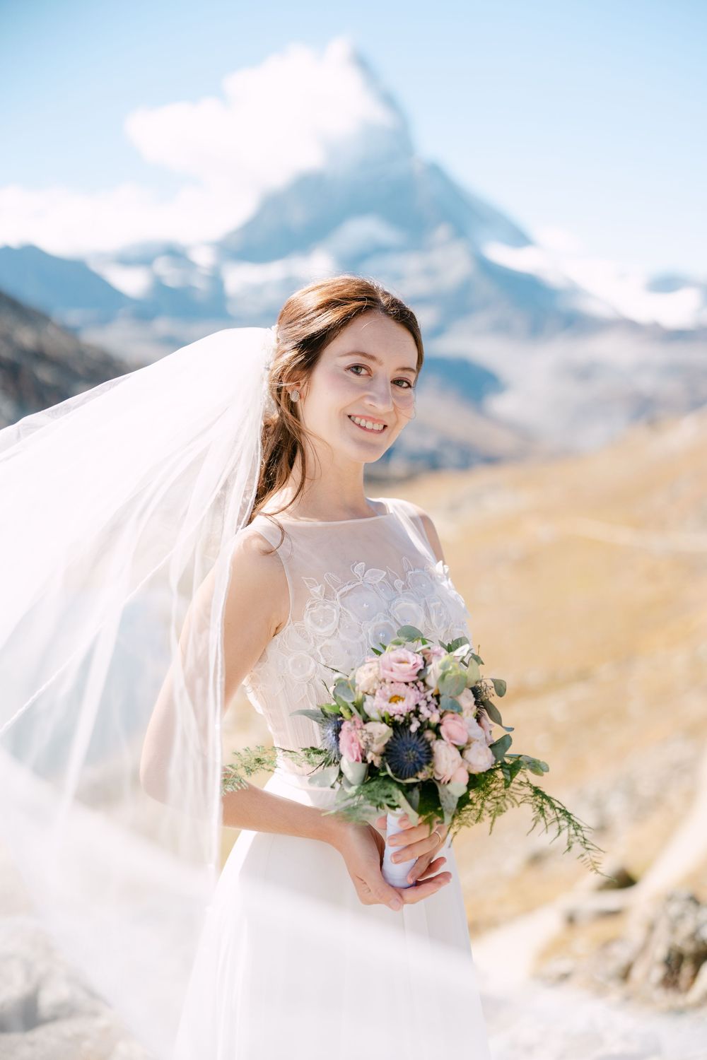 Scenic mountain wedding photography series with flowing veil and pink floral bouquet against snow-capped alpine peaks in Zermatt.